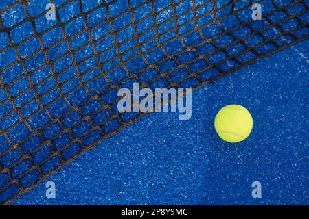 Paddeln Sie mit dem Tennisball in der Nähe des Netzes eines blauen Platzes. Ball neben dem Netz eines blauen Paddle-Tennisplatzes. Ball neben dem Netz eines blauen Paddle-Tennis-Cours Stockfoto