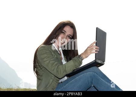 Frau, die Freiberuflerin, die auf einer hohen Klippe über dem Meer sitzt und aus der Ferne arbeitet Stockfoto