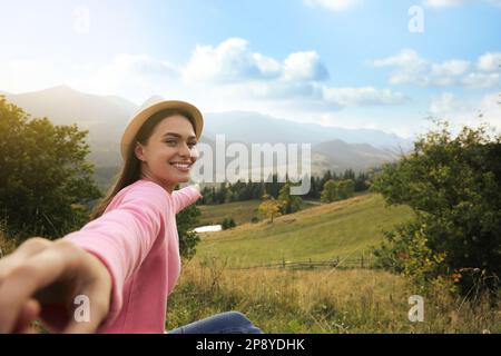 Junge Frau, die die Hand ihres Freundes in den Bergen hält, Platz für Text Stockfoto