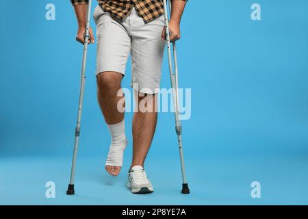 Junger Mann mit verletztem Bein mit Axillarkrücken auf hellblauem Hintergrund, Nahaufnahme Stockfoto