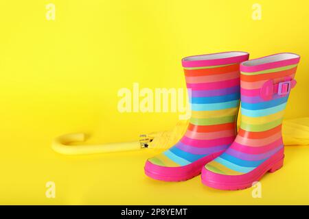 Gestreifte Gummistiefel neben dem Regenschirm auf gelbem Hintergrund. Platz für Text Stockfoto