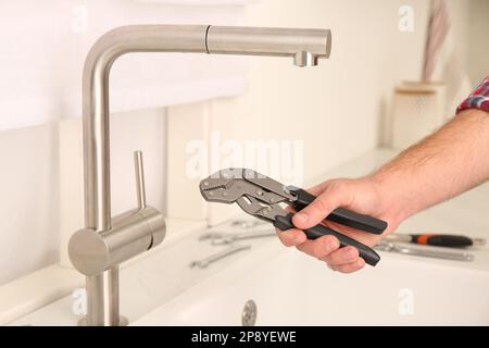 Mann mit Schraubenschlüssel neben Waschbecken in der Küche, Nahaufnahme. Installation des Wasserhahns Stockfoto