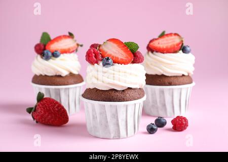 Köstliche Cupcakes mit Sahne und Beeren auf pinkfarbenem Hintergrund Stockfoto