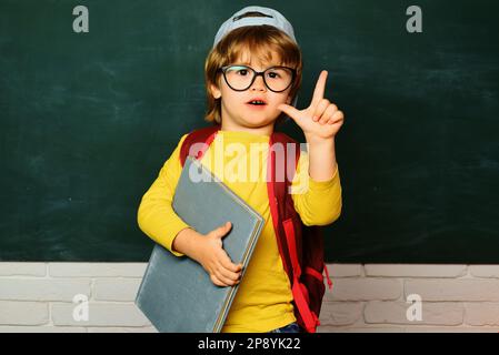 Nette kleine Vorschule Junge in einem Klassenzimmer. Private Schule. Bereit für die Schule. Bildungsprozess. Lustiger kleiner Junge, der auf Tafel zeigt. Stockfoto