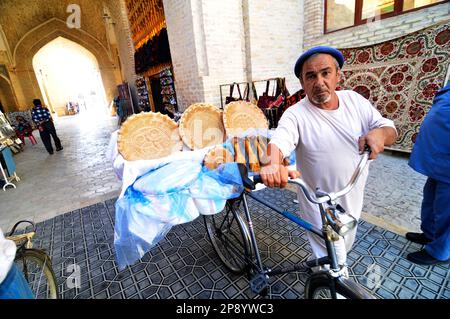 Ein usbekischer Mann, der frisches Obi-Non-Brot von seinem Fahrrad in der Altstadt von Bukhara, Usbekistan, verkauft. Stockfoto