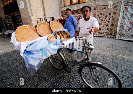 Ein usbekischer Mann, der frisches Obi-Non-Brot von seinem Fahrrad in der Altstadt von Bukhara, Usbekistan, verkauft. Stockfoto