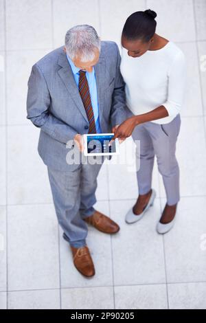 Die Verwaltung von Projekten war noch nie so einfach. Aufnahme aus einem hohen Winkel von zwei Kollegen, die mit einem digitalen Tablet stehen. Stockfoto