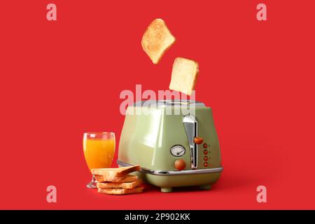 Moderner Toaster mit knusprigen Brotscheiben und einem Glas Saft auf rotem Hintergrund Stockfoto