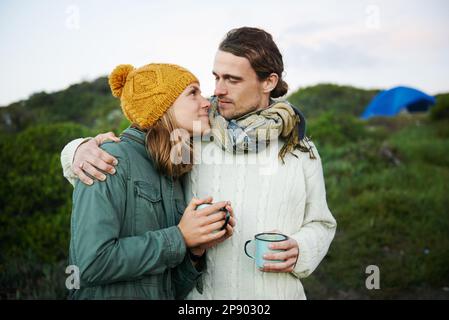 Sich in den Augen der anderen zu verirren. Ein liebevolles junges Paar, das draußen mit heißen Getränken steht. Stockfoto