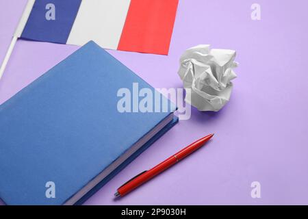 Französische Flagge mit Notizbuch, Stift und zerknittertem Papier auf lila Hintergrund, Nahaufnahme Stockfoto