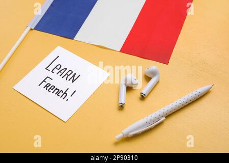 Papier mit Text LERNE FRANZÖSISCH, Kopfhörer, Stift und Flagge von Frankreich auf gelbem Hintergrund, Nahaufnahme Stockfoto