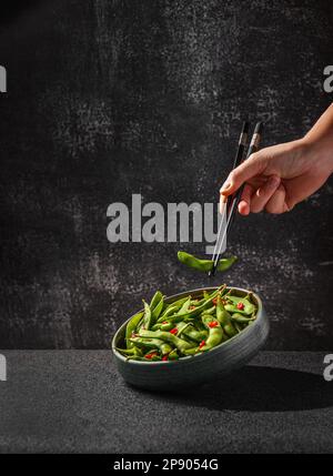 Edamamabohnensalat in Hülsen mit Chili-Pfeffer auf schwarzem Hintergrund Stockfoto