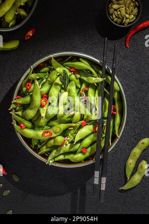 Edamamabohnensalat in Hülsen mit Chili-Pfeffer auf schwarzem Hintergrund Stockfoto