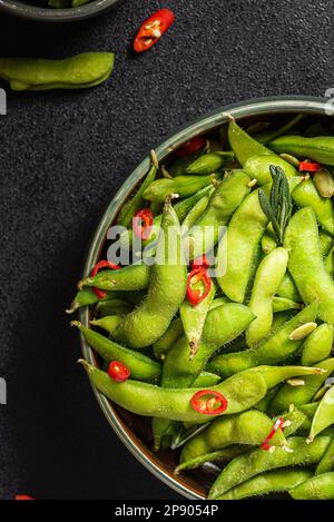 Edamamabohnensalat in Hülsen mit Chili-Pfeffer auf schwarzem Hintergrund Stockfoto