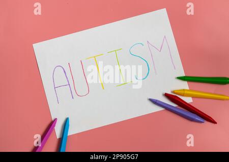 Textwort Autismus auf Papierbogen mit bunten Buchstaben auf blauem Hintergrund. Stockfoto