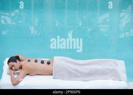 Es gibt keine bessere Art, sich zu entspannen. Eine attraktive Frau, die auf einem Massagetisch am Pool lag. Stockfoto