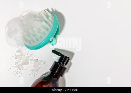 Haarbürste für Kopfmassage und Reinigung mit Schaum, eine Flasche Shampoo auf weißem Hintergrund mit scharfen Schatten Stockfoto