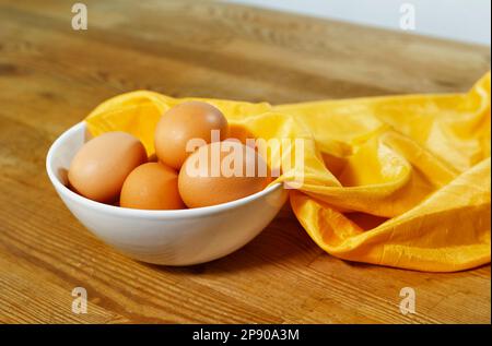 Hühnereier in einer weißen Schüssel auf einem Holztisch, Zubereitung von Essen, Stockfoto