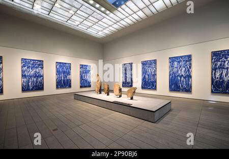 Ein Galerieraum, der modernen, blauen Gemälden gewidmet ist, und eine Skulptureninstallation aus Stein. Im Kunstmuseum des französischen Louvre in Abu Dhabi, Vereinigte Arabische Emirate, Stockfoto