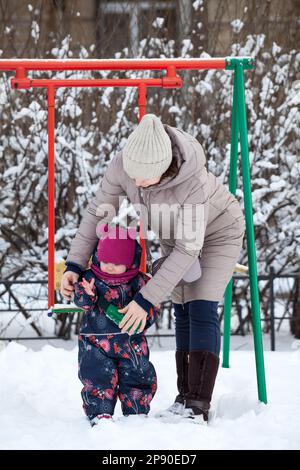 Mom hilft einem kleinen Kind, Fäustlinge an den Händen zu tragen, Wintersaison Stockfoto