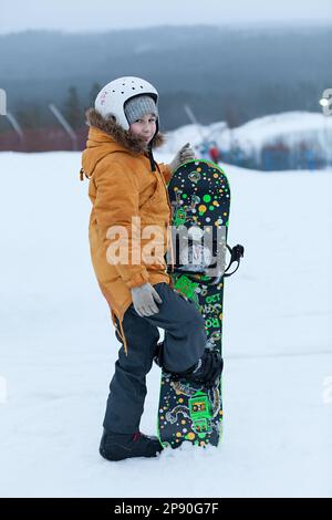 St. Petersburg, Russland-circa Januar 2018: Ein achtjähriges Mädchen trägt einen Helm in einem Skigebiet. Posen mit Snowboard Stockfoto