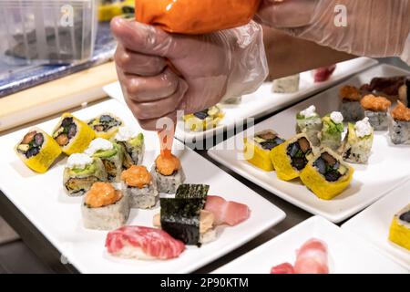 Ein unbekannter Koch in Handschuhen, der köstliches Sushi mit Sauce serviert, während er das Essen im Restaurant zubereitet Stockfoto