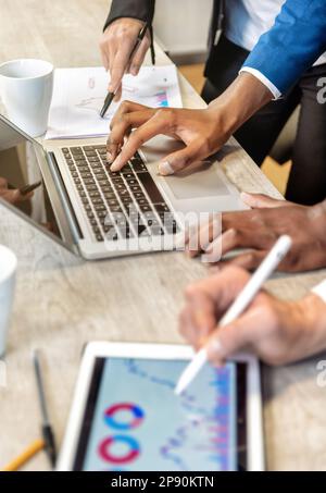 Von oben: Anonyme Mitarbeiter, die an der Geschäftsstrategie arbeiten, verwenden Laptops und Tablets mit Diagrammen während der Zusammenarbeit im Büro Stockfoto
