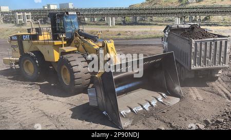 Radlader, der Kohle auf Lkw lädt und auf einer riesigen Bergbaustelle arbeitet. Stockfoto