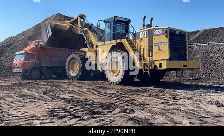 Radlader, der Kohle auf Lkw lädt und auf einer riesigen Bergbaustelle arbeitet. Stockfoto