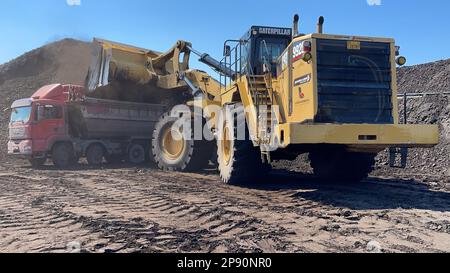 Radlader, der Kohle auf Lkw lädt und auf einer riesigen Bergbaustelle arbeitet. Stockfoto