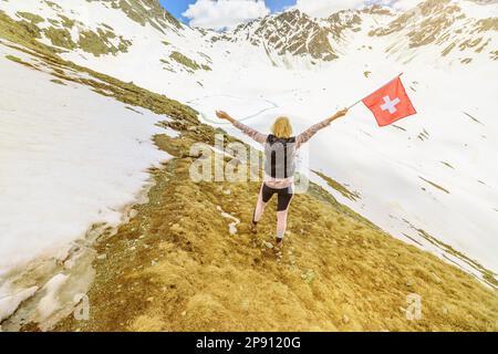 Eine Touristenfrau mit schweizer Flagge im Schnee auf dem Muottas-Muragl-Berg der Schweiz. Beliebte Bergausflüge im Kanton Graubunden Stockfoto