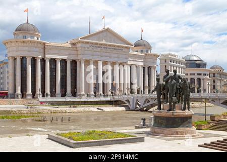 Skopje, Nordmekedonien - Mai 21 2019: Denkmal der Bootsatmer von Thessaloniki mit dem Archäologischen Museum von Mazedonien gegenüber der Brücke von Civi Stockfoto