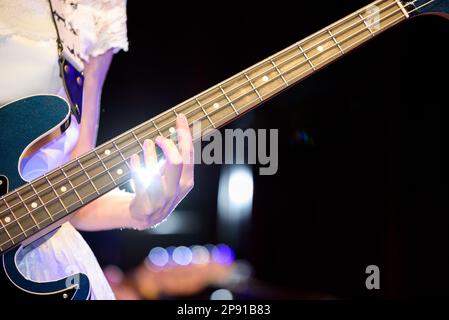 Musikerin in einem weißen Kleid, die elektrische Bassgitarre spielt. Nahaufnahme der Hand. Stockfoto