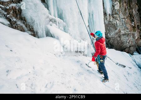 Eiskletterer kleidete warme Winterkletterkleidung, Sicherheitsgeschirr und Helm unter dem gefrorenen Wasserfall. Konzept für aktive Menschen und sportliche Aktivitäten im Stockfoto