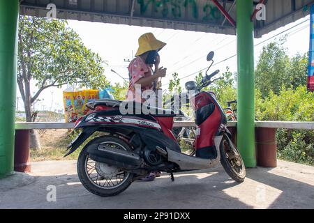 BANGKOK, THAILAND, FEBRUAR 07 2023, Eine Frau mit Taschen parkt ihr Motorrad in einer öffentlichen Bushaltestelle und fährt mit dem Bus. Stockfoto