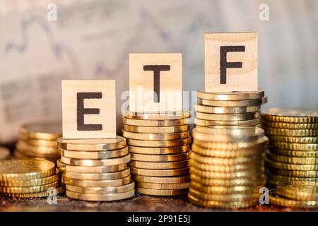 Mehrere Stapel mit Münzen und der Bezeichnung ETF und ein Diagramm mit Aktienkursen. Stockfoto