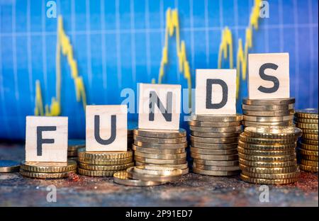 Mehrere Münzstapel und der Begriff "Fonds" und eine Tabelle mit Aktienkursen. Stockfoto