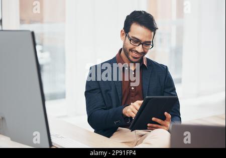 Büro, glücklicher indischer Mann am Schreibtisch mit Tablet und Computer, liest gute Nachrichten-E-Mails oder erfolgreiche Verkaufsberichte online. Geschäft, Lächeln und Stockfoto