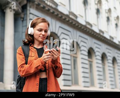 Frau mit Kopfhörern kommuniziert über ihr Mobiltelefon im Internet. Stockfoto