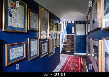 Blaue Wände in Oxford im Flur mit Fotografien von Cecil Beaton und Zeichnungen von Stephen Tennant im Tudor-Bauernhaus aus dem 16. Jahrhundert in Suffolk, Großbritannien Stockfoto