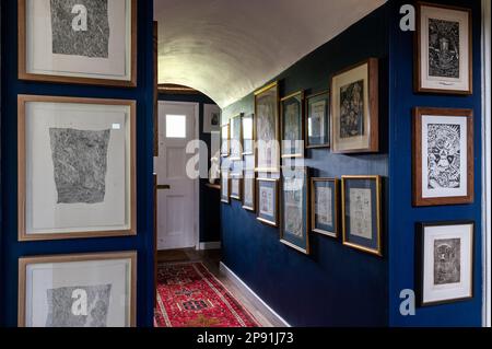 Blaue Wände in Oxford im Flur mit Kunstwerken von Cecil Beaton, Stephen Tennant und Viktor Wynd. 16. Century Tudor Farmhouse, Suffolk, Großbritannien. Stockfoto
