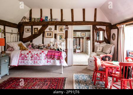 Patchwork-Steppdecke auf dem Bett mit Spielzeug in einem Mädchenschlafzimmer mit Holzrahmen. 16. Century Tudor Farmhouse, Suffolk, Großbritannien. Stockfoto