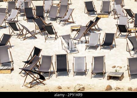 Landschaftlich schöner Blick auf das Wasser von vielen leeren schwarzen Holzliegen auf dem Sandfluss oder dem Meeresstrand. Reihen von Liegestühlen an geschlossener Küste aufgrund von Kontamination Stockfoto