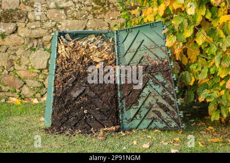 Der Kompostbehälter für den Außenbereich wurde geöffnet, um reifen Kompost aus dem unteren Teil zu extrahieren. Der Kompostbehälter wird in einen Garten gestellt, um organischen Abfall zu recyceln Stockfoto