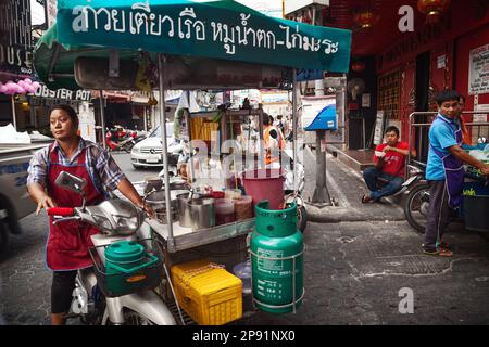Pattaya, Thailand - 28. März 2016: Asiatische Frau, die einen Imbisswagen fährt und Straßenessen verkauft. Mobiler thailändischer Lebensmittelhändler. Text auf einem Wagen: Nudeln mit Schweinefleisch, Stockfoto