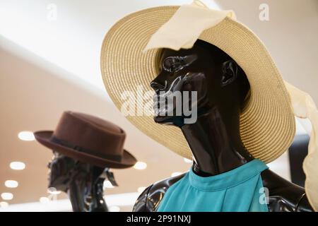 Traurige Dame Normpuppe trägt einen Strohhut in einem Schaufenster. Nachdenklich mannequin Frau präsentiert Sommer mode Stil in einem Bekleidungsgeschäft Stockfoto