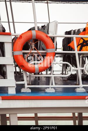 Rettungsring und Schwimmwesten auf einer Fähre deck Nahaufnahme. Rettungsgeräte auf einem Schiff: Boje und Unterhemden für Notfälle Stockfoto