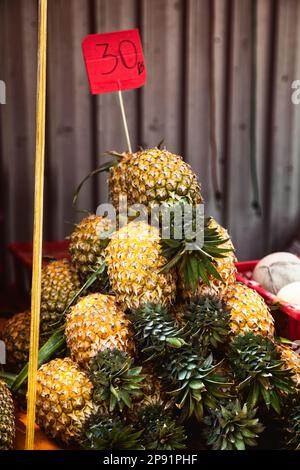 Haufen von ungeschälte Ananas mit Preisschild an der Markt-Theke. Viele gelbe Frucht gestapelt in einer Pyramide in Thailand im Supermarkt Stockfoto