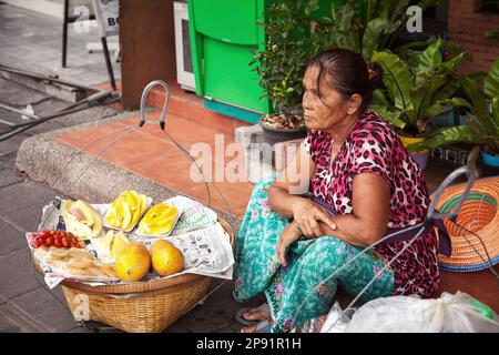 Pattaya, Thailand - 28. März 2016: Thailändischer Straßenverkäufer, der Obst aus Körben verkauft. Lebensmittelverkäufer sitzt auf dem Bürgersteig Stockfoto