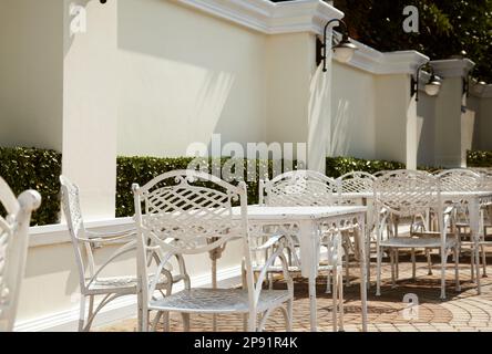 Leere outdoor-Café im Hotel. Schmiedeeiserne Möbel - Reihe von weißen Tische mit Stühlen Stockfoto